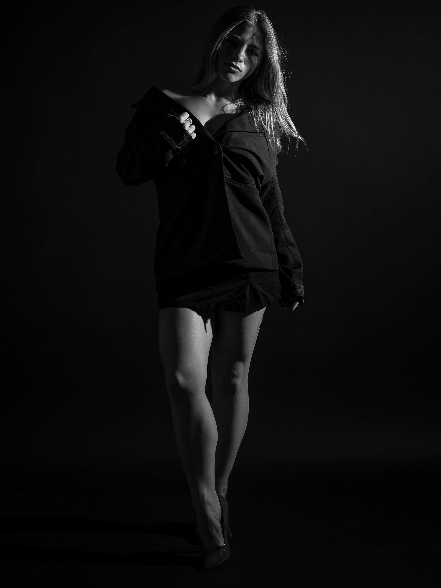 Black and white photo of a woman in a dark oversized top and shorts posing confidently against a dark background.