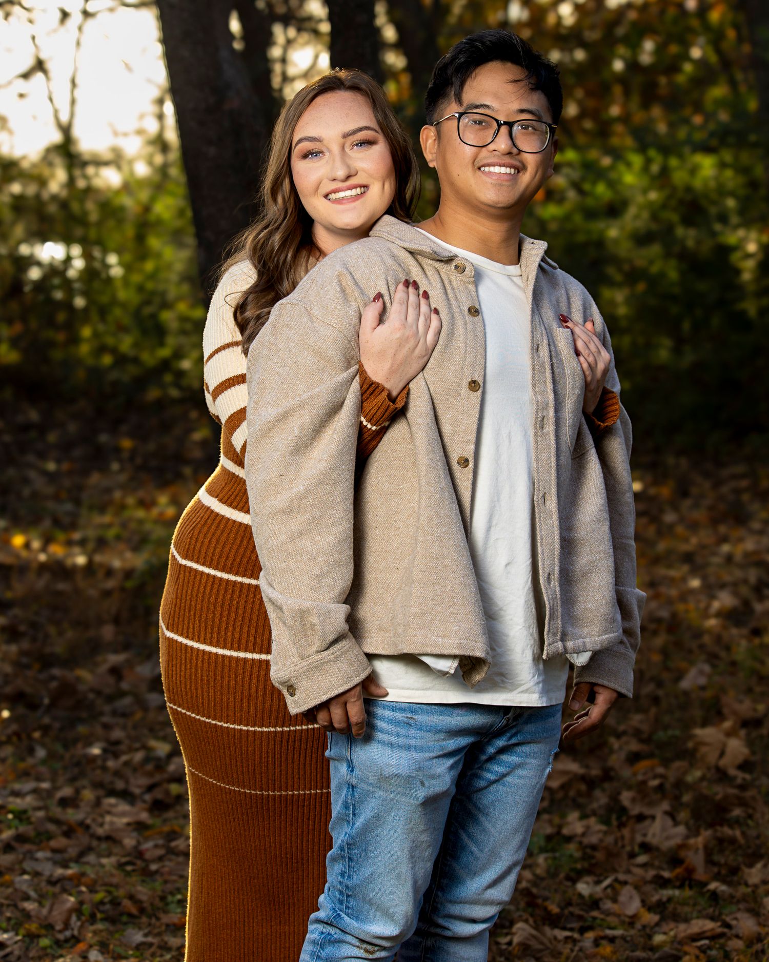 A couple shares a joyful moment together in a wooded area during an autumn photo session.