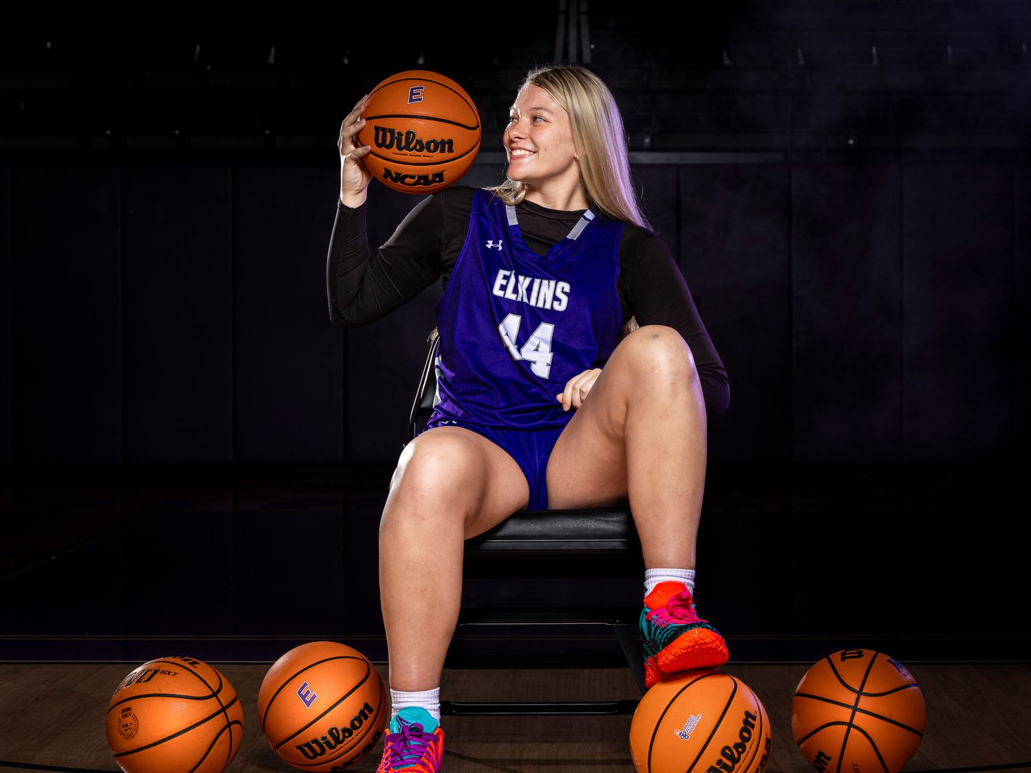 Female basketball player in Elkins #4 jersey posing with Wilson basketballs in a professional sports photo shoot.