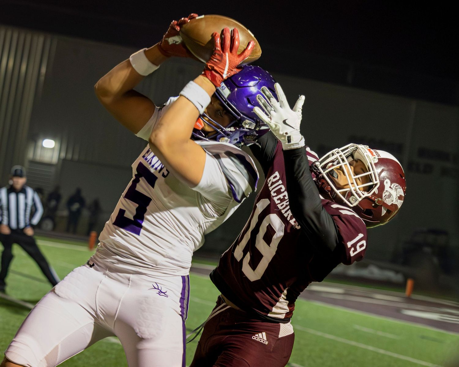 Two football players from opposing teams compete for control of the ball during an intense game play.
