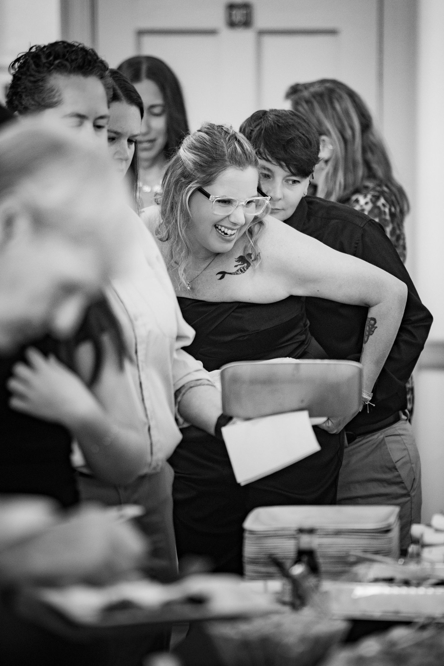Black and white photo showing a lively group of people laughing and socializing at a gathering.