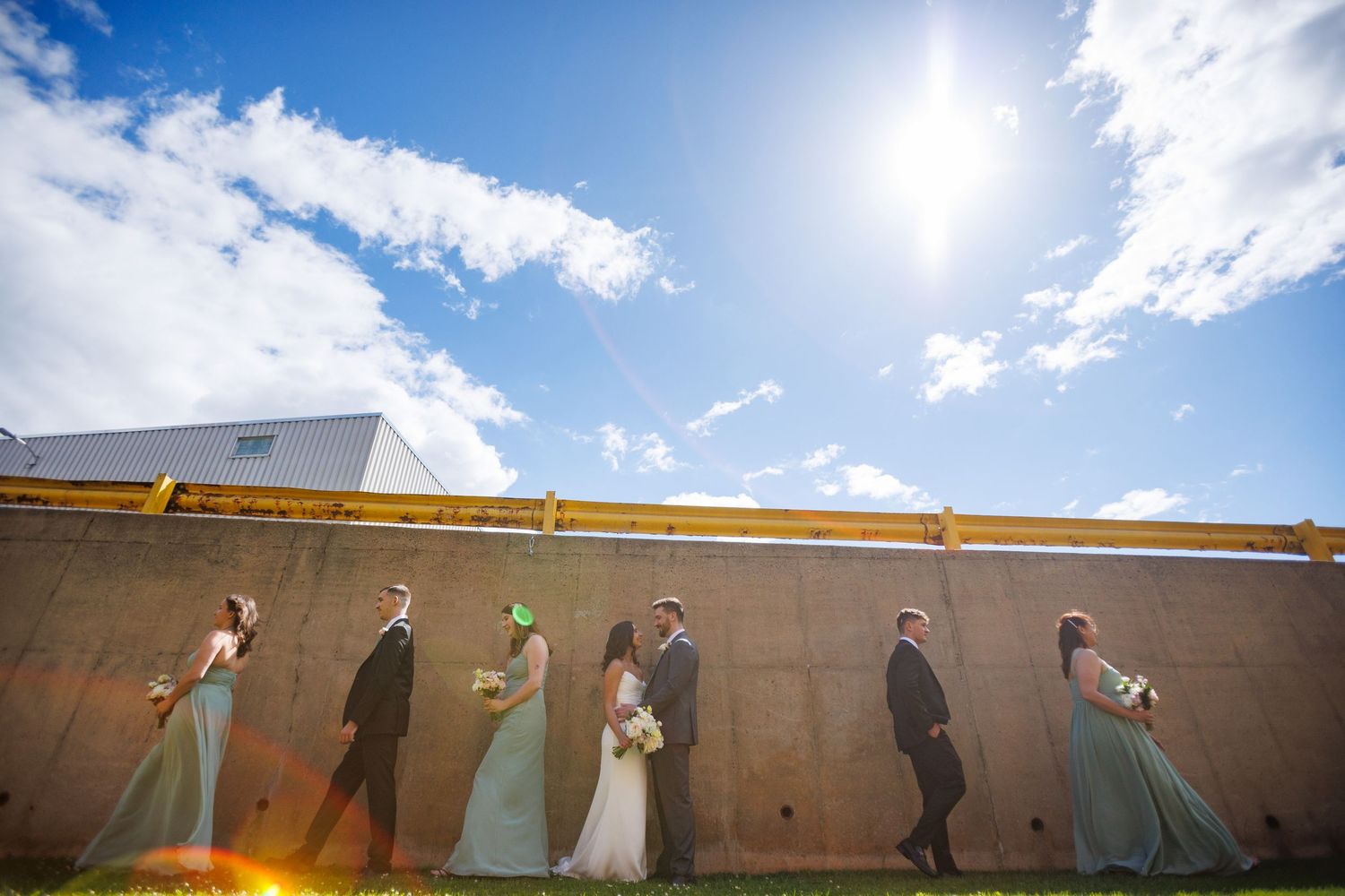 Wedding party poses against a golden wall under a bright blue sky, with bridesmaids in mint gowns and groomsmen in suits.