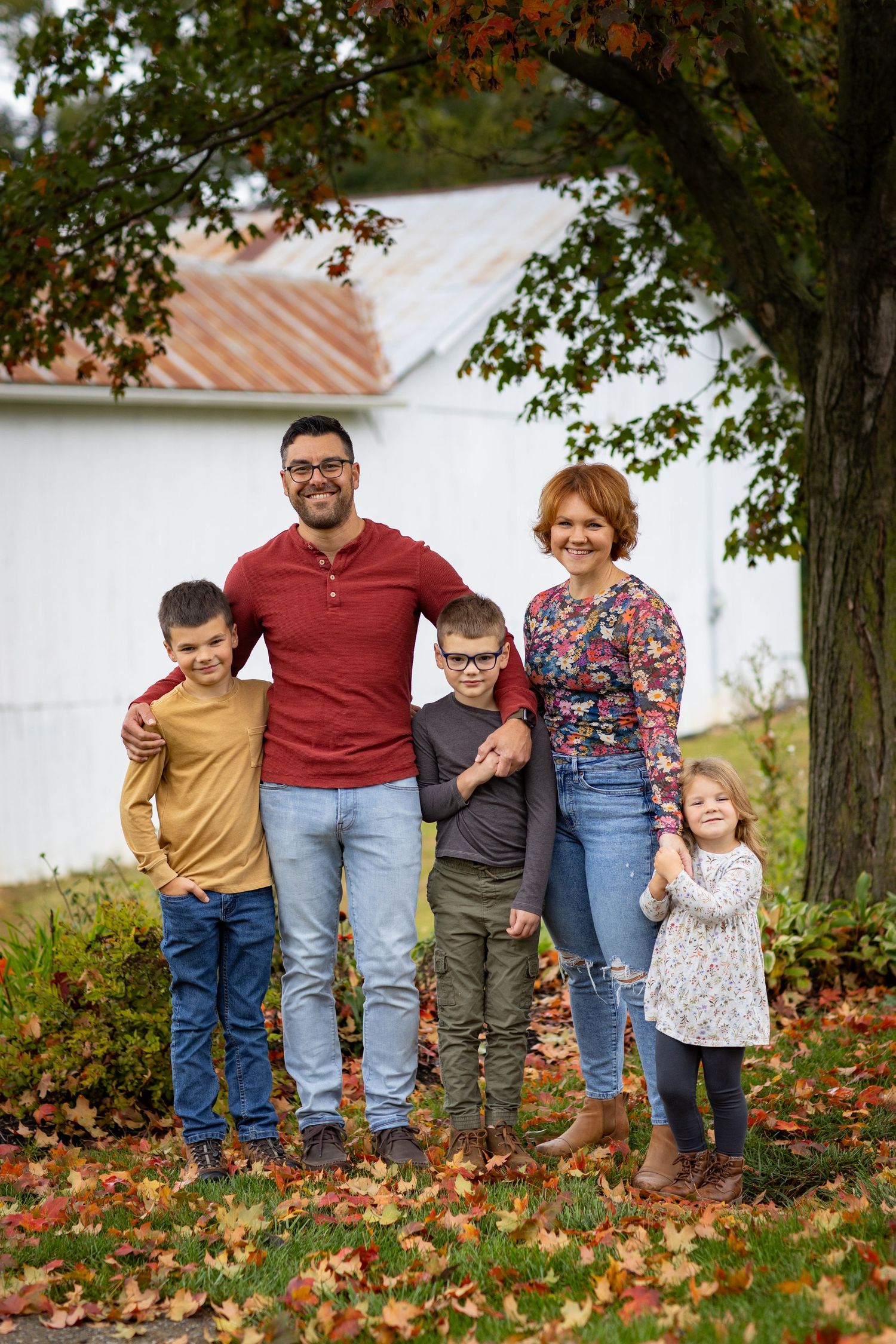 Family members stand together among fallen autumn leaves near a white building.