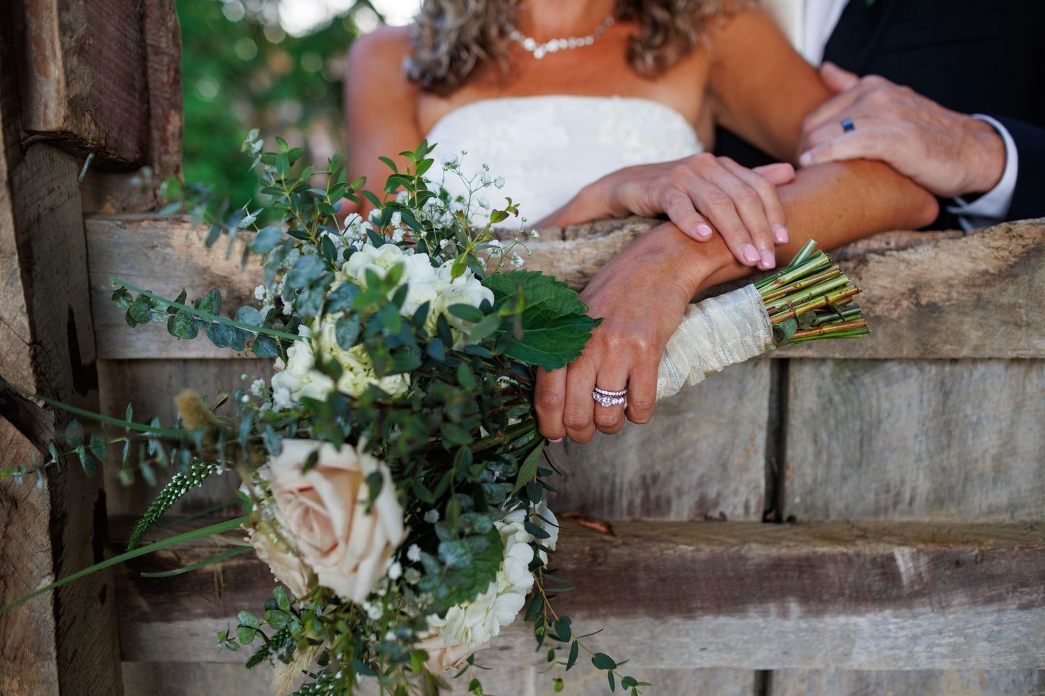 Newlyweds display wedding rings while holding a bridal bouquet of white flowers and eucalyptus greenery.