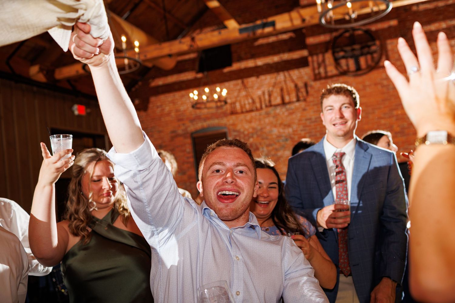 Enthusiastic wedding guest cheering with raised arm on the dance floor at a lively reception.