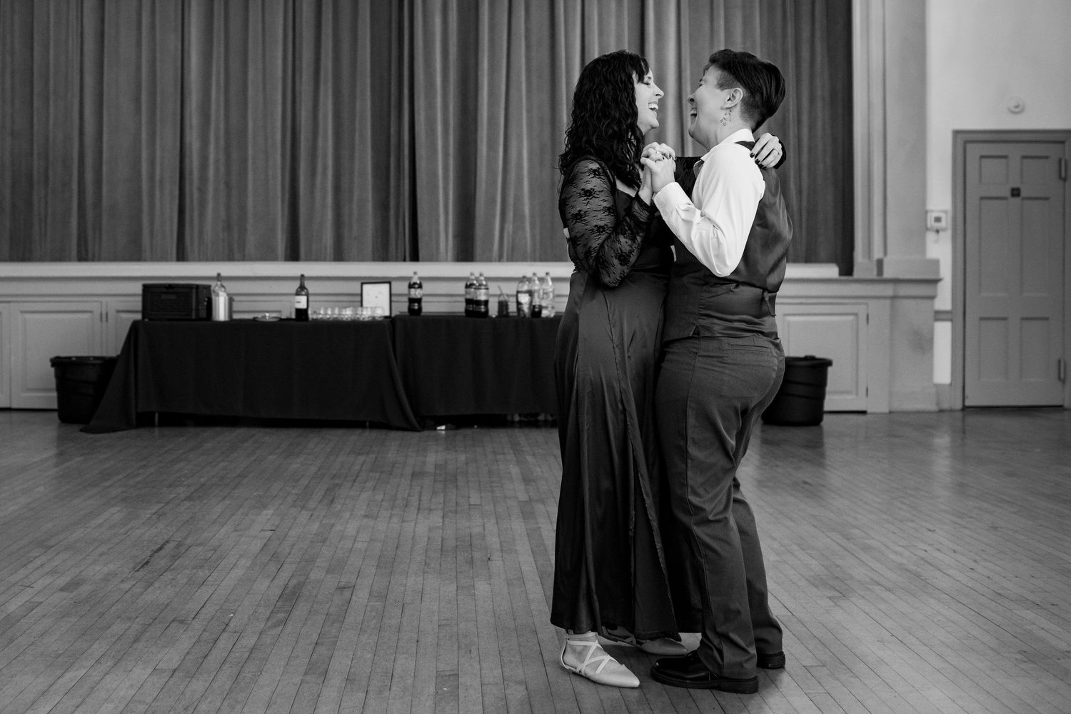 Black and white image of people interacting at a formal event in a room with hardwood floors.