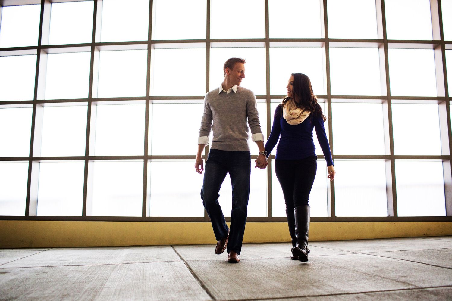 Silhouetted couple holding hands against large window backdrop.