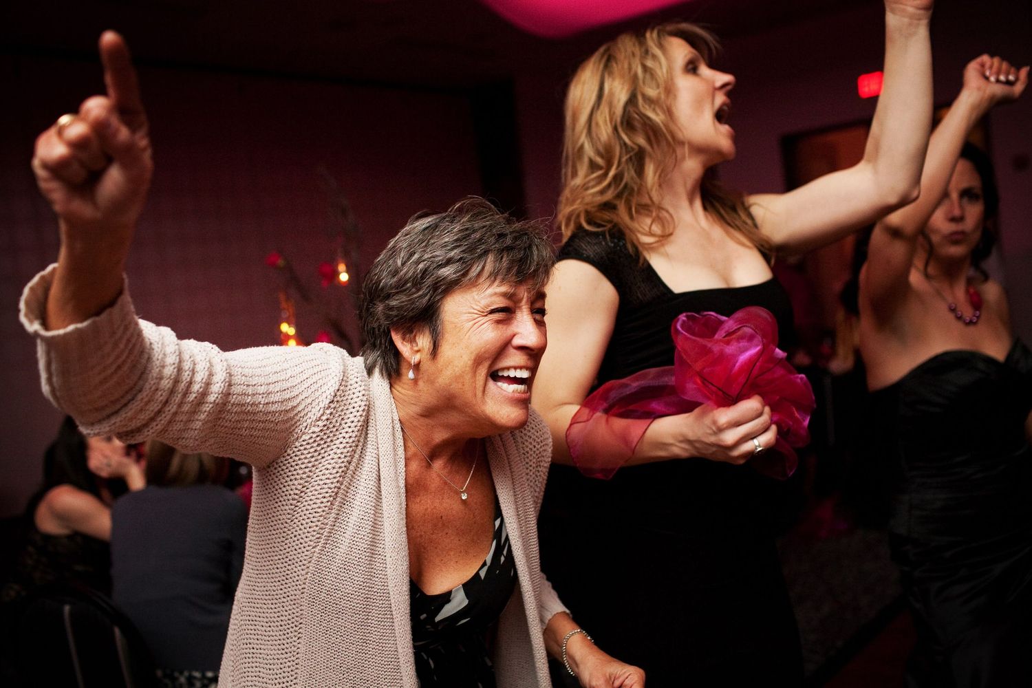 People dancing and celebrating energetically at a party with smiles and raised arms under dark lighting.