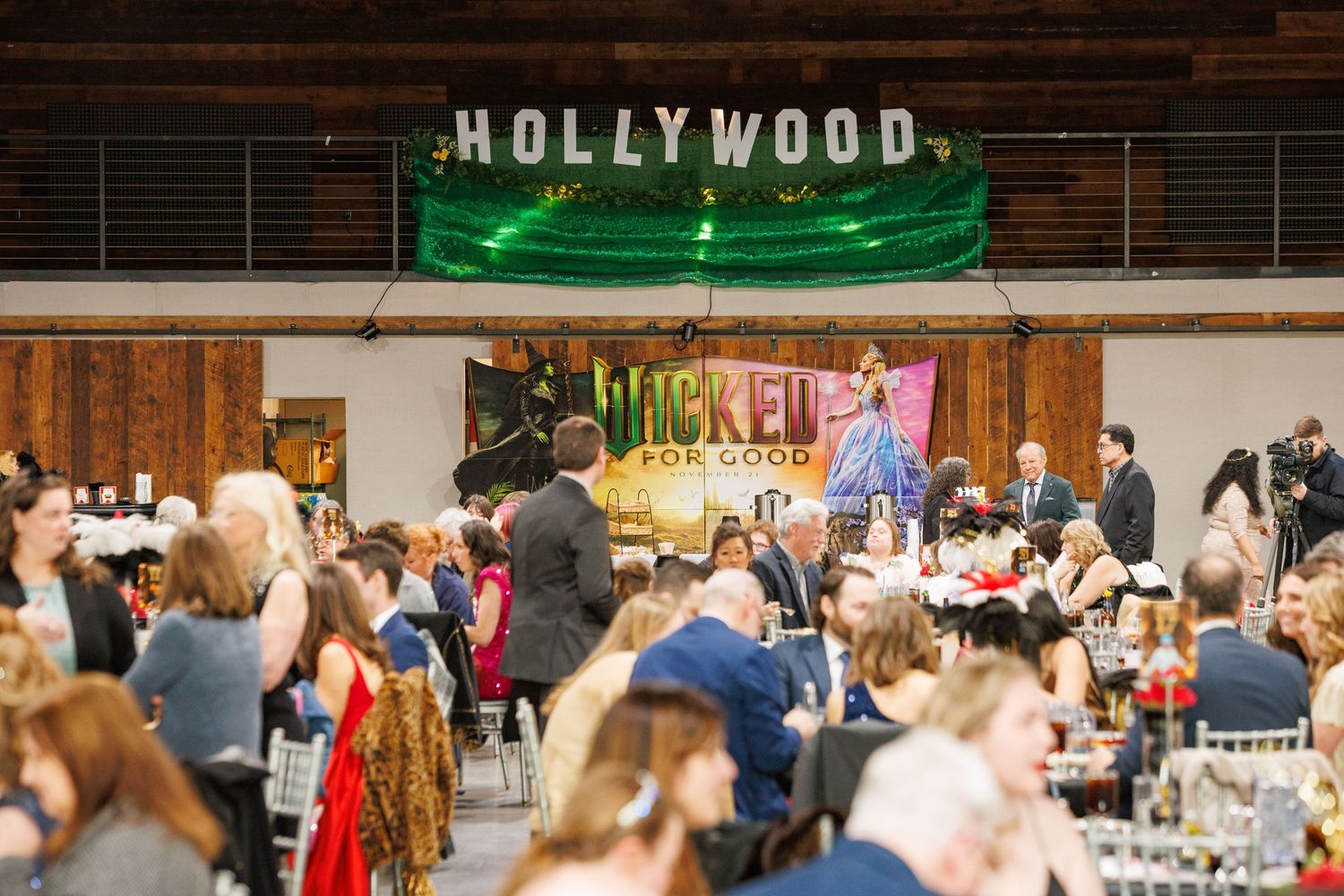 Hollywood-themed gala event with guests dining under a green banner at a Wicked For Good charity banquet.