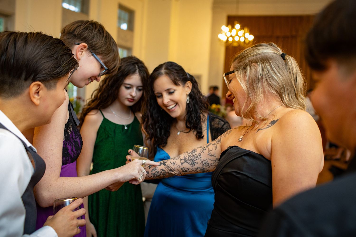 A group of wedding guests gather together in a candid moment at a reception venue with warm lighting.