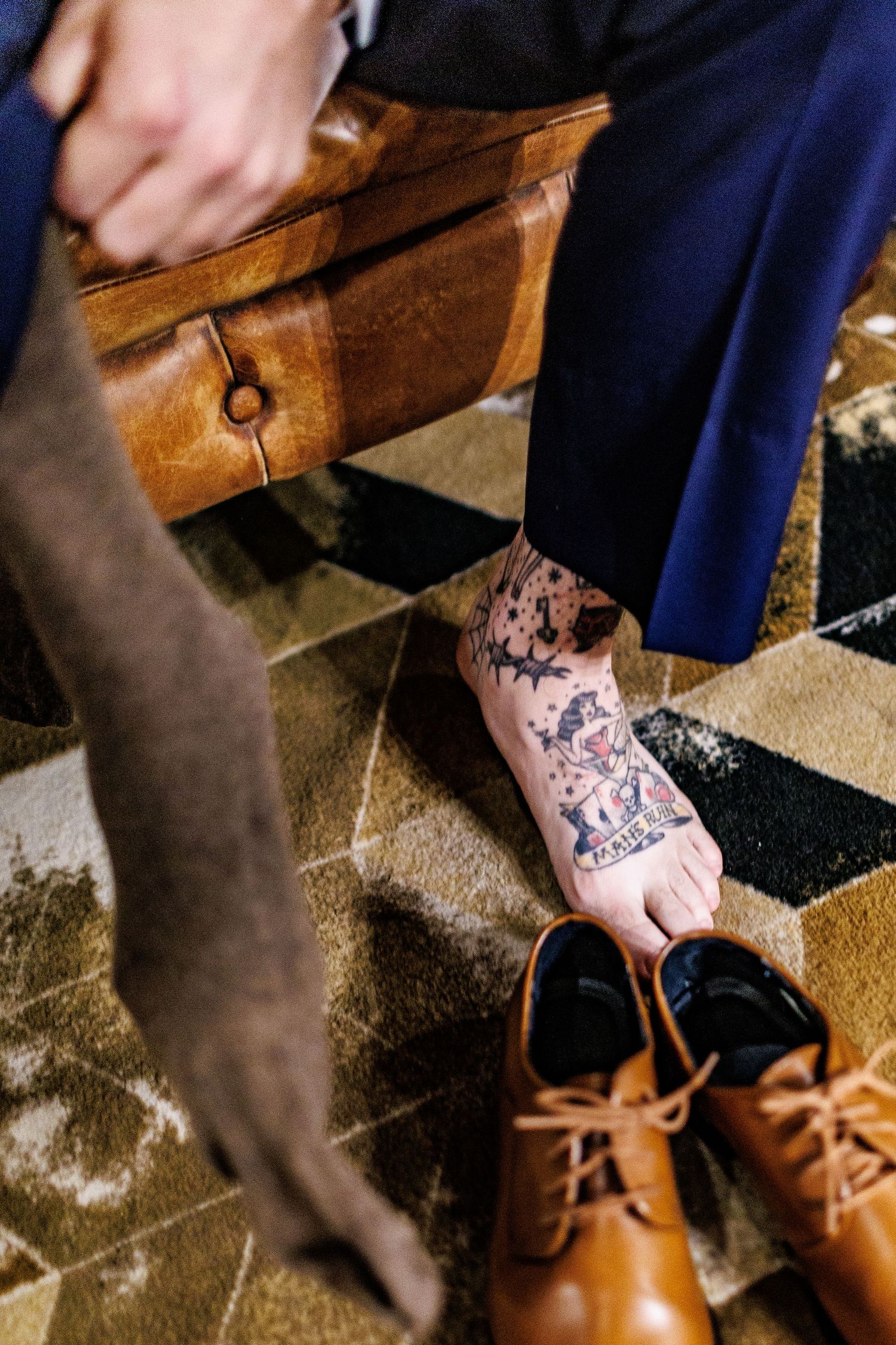 Close-up of brown leather dress shoes and tattooed feet being put on before formal event.