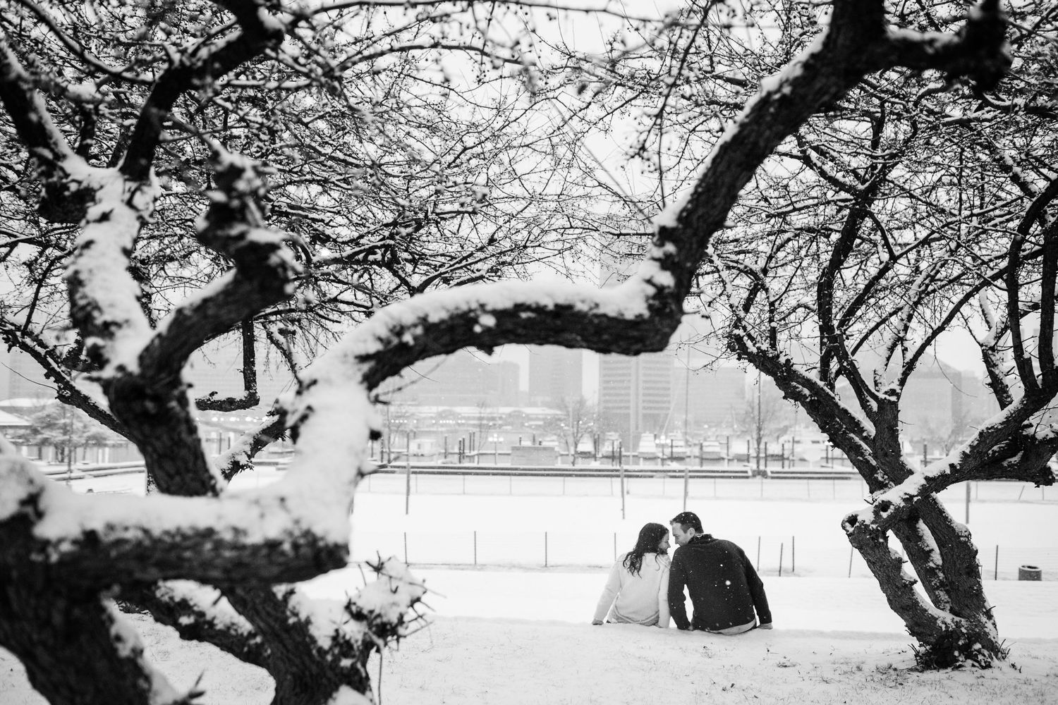 Couple sits together under snow-covered trees in winter landscape.