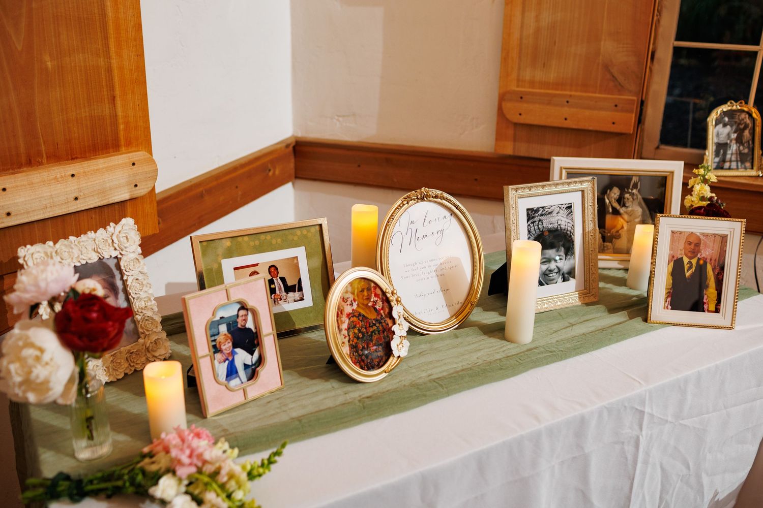 Wedding memorial table with framed family photos, candles, and floral arrangements displayed on a white cloth-covered surface.