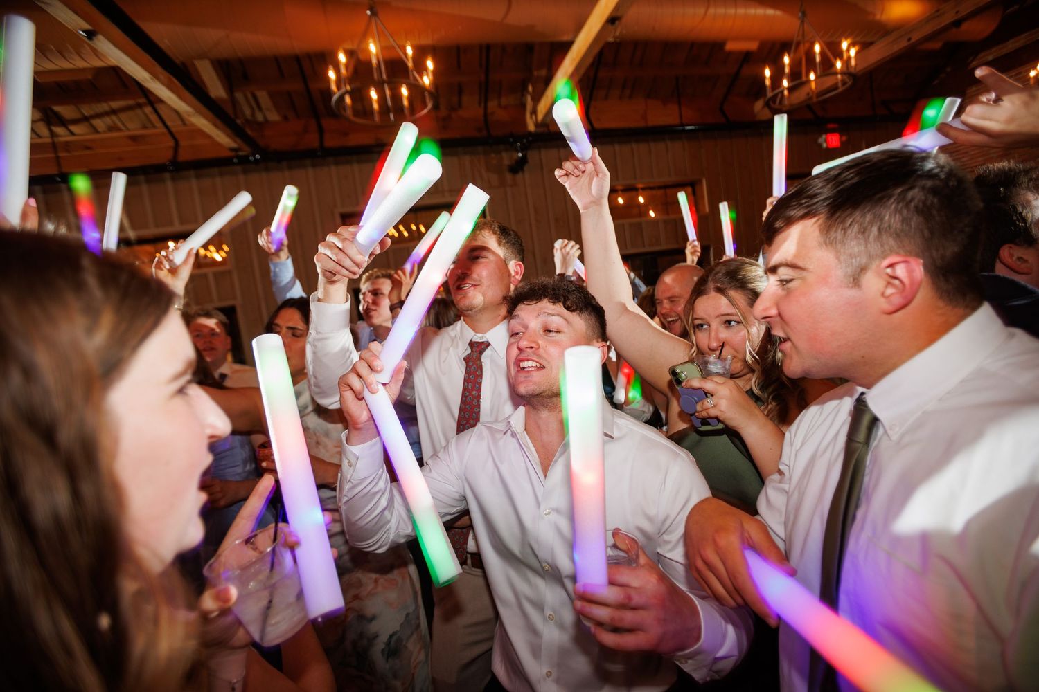Excited wedding guests wave colorful LED glow sticks on the dance floor during evening reception.