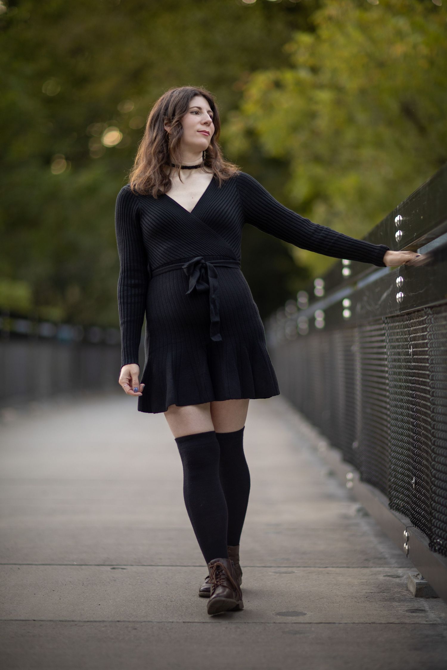Person in black dress sits gracefully on wooden bridge walkway surrounded by autumn foliage and natural scenery.