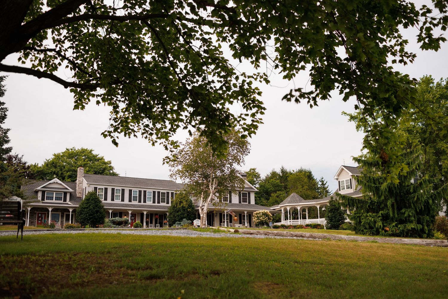 Elegant gray colonial estate surrounded by lush green lawns and mature trees on an overcast day.