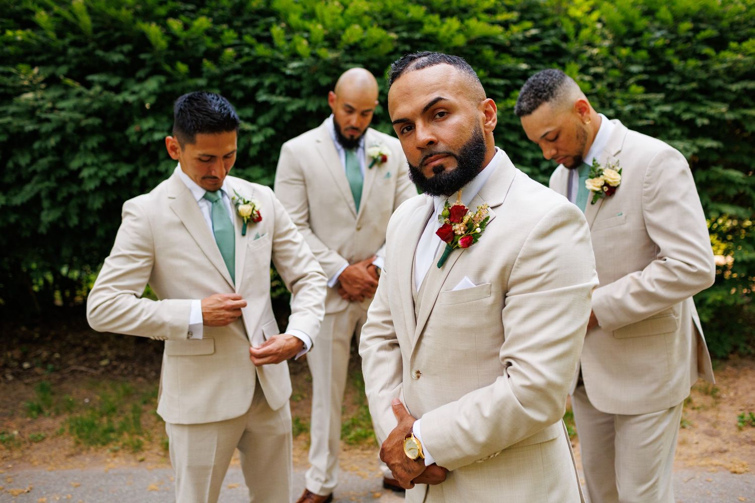 Groom and groomsmen posing in matching beige suits with floral boutonnieres outdoors.