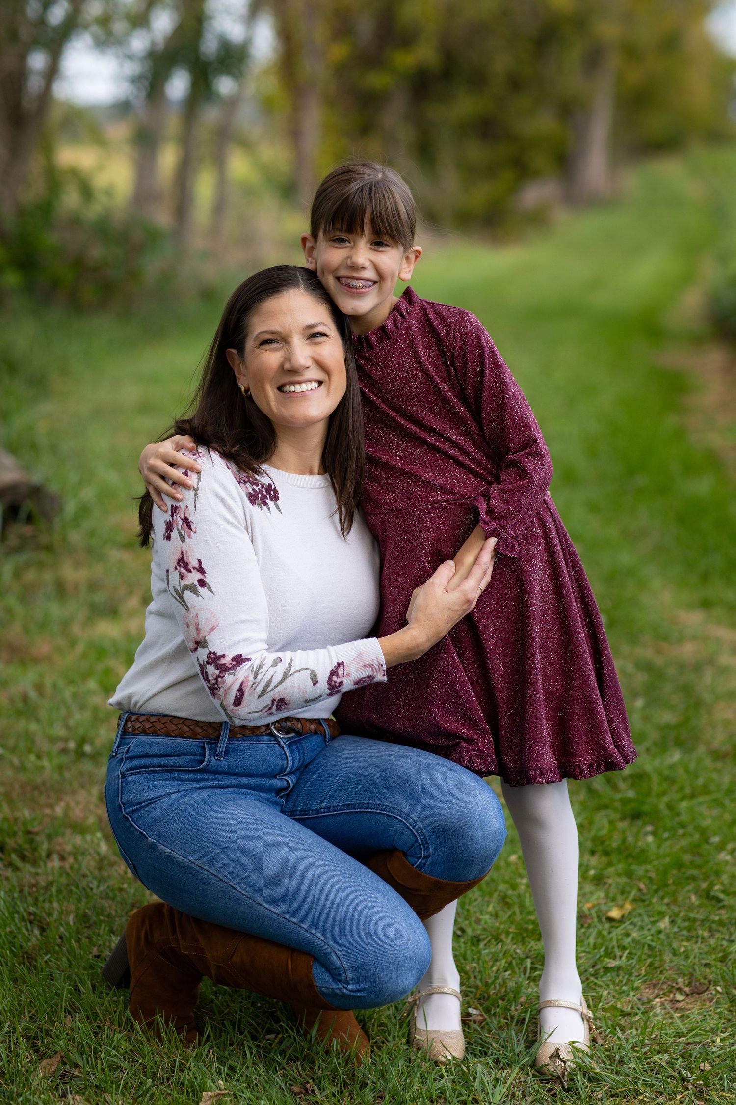 A couple sitting together on grass in a park setting wearing burgundy and white tops with blue jeans.