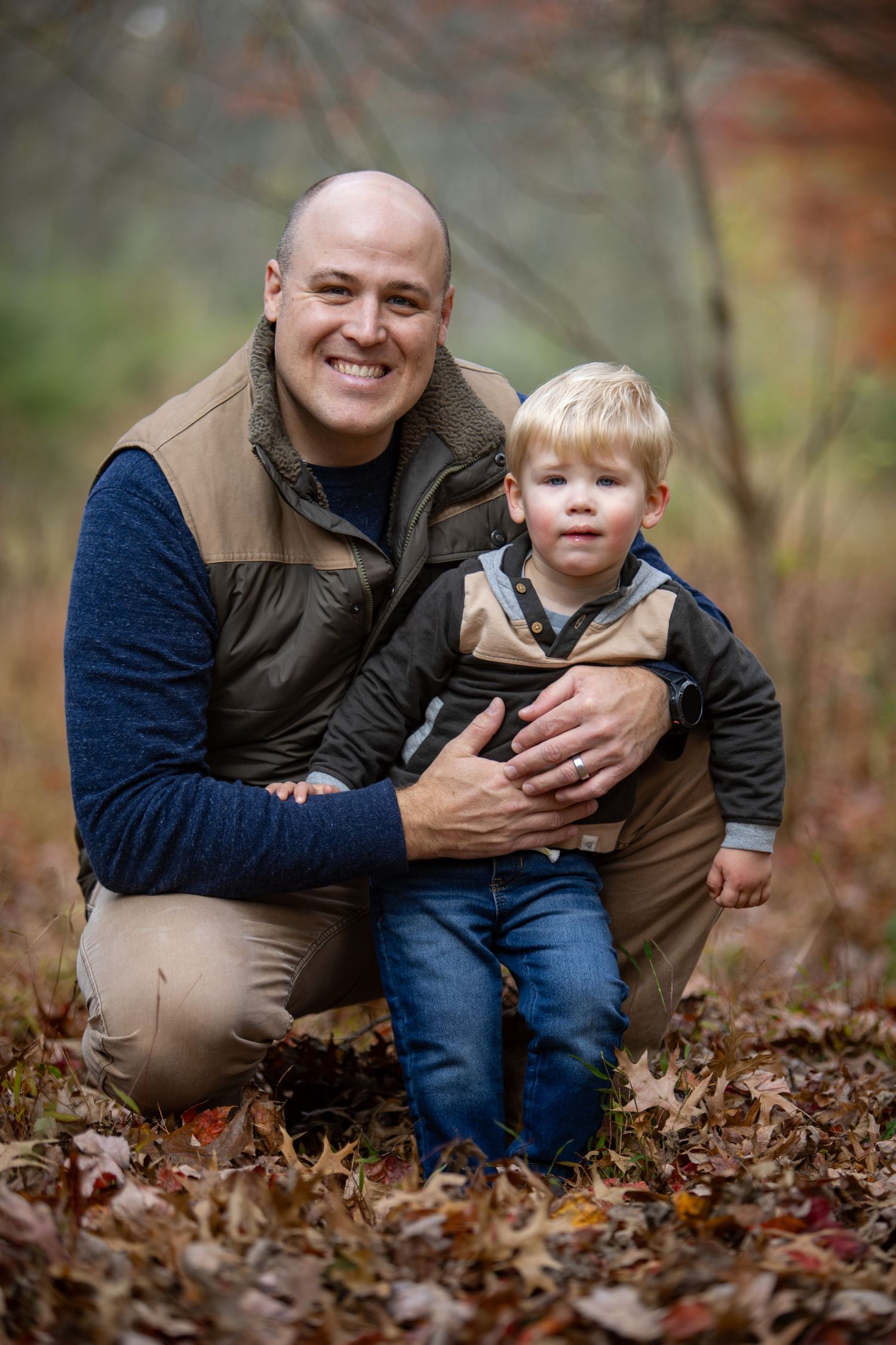 A parent and child share tender moments while sitting among fallen autumn leaves in an outdoor photo series.
