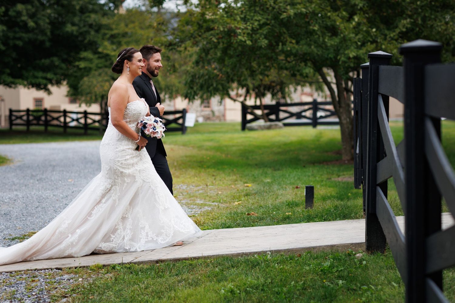 Couple in wedding attire walking along a scenic lakeside path.