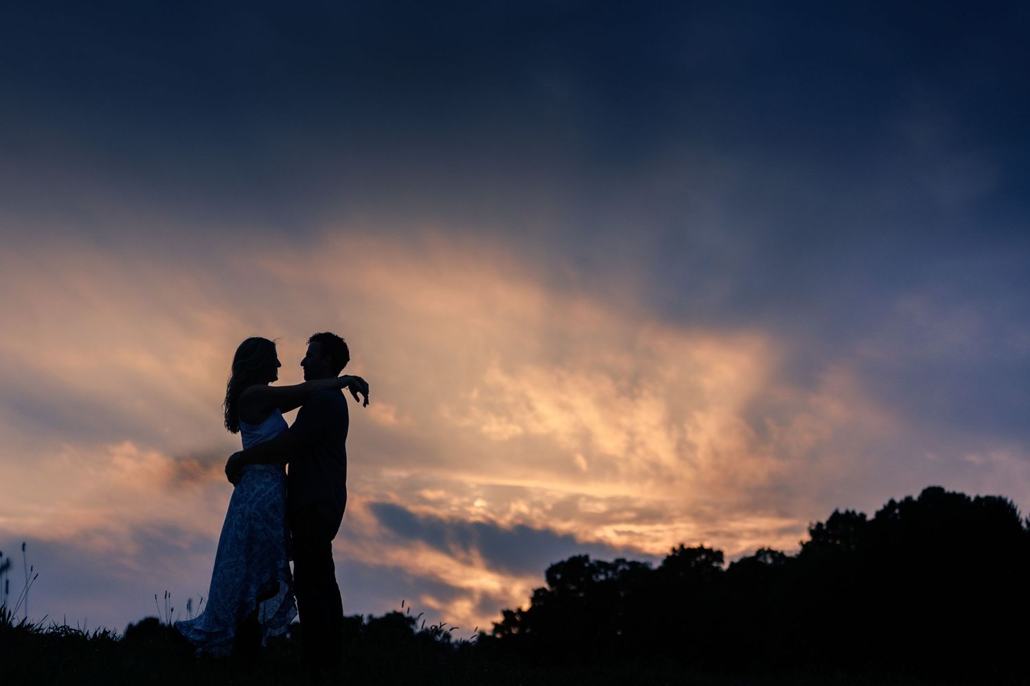 Silhouette of a romantic couple embracing against a dramatic sunset sky with glowing orange and purple clouds.