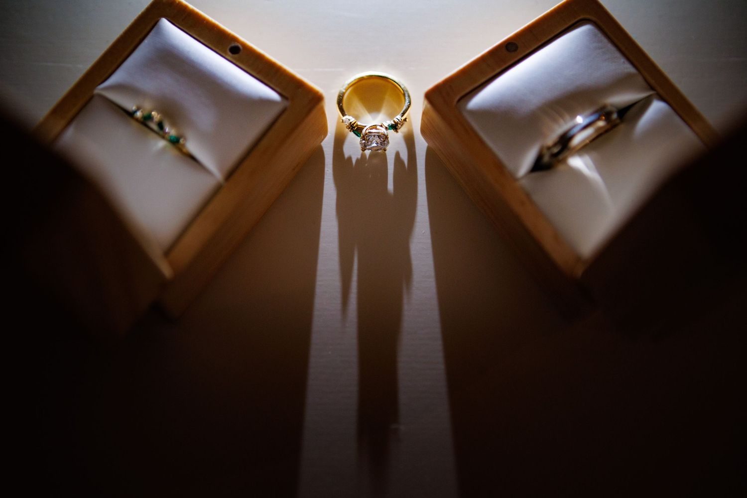 Three wedding rings displayed in wooden boxes with dramatic shadows cast on a dark surface.