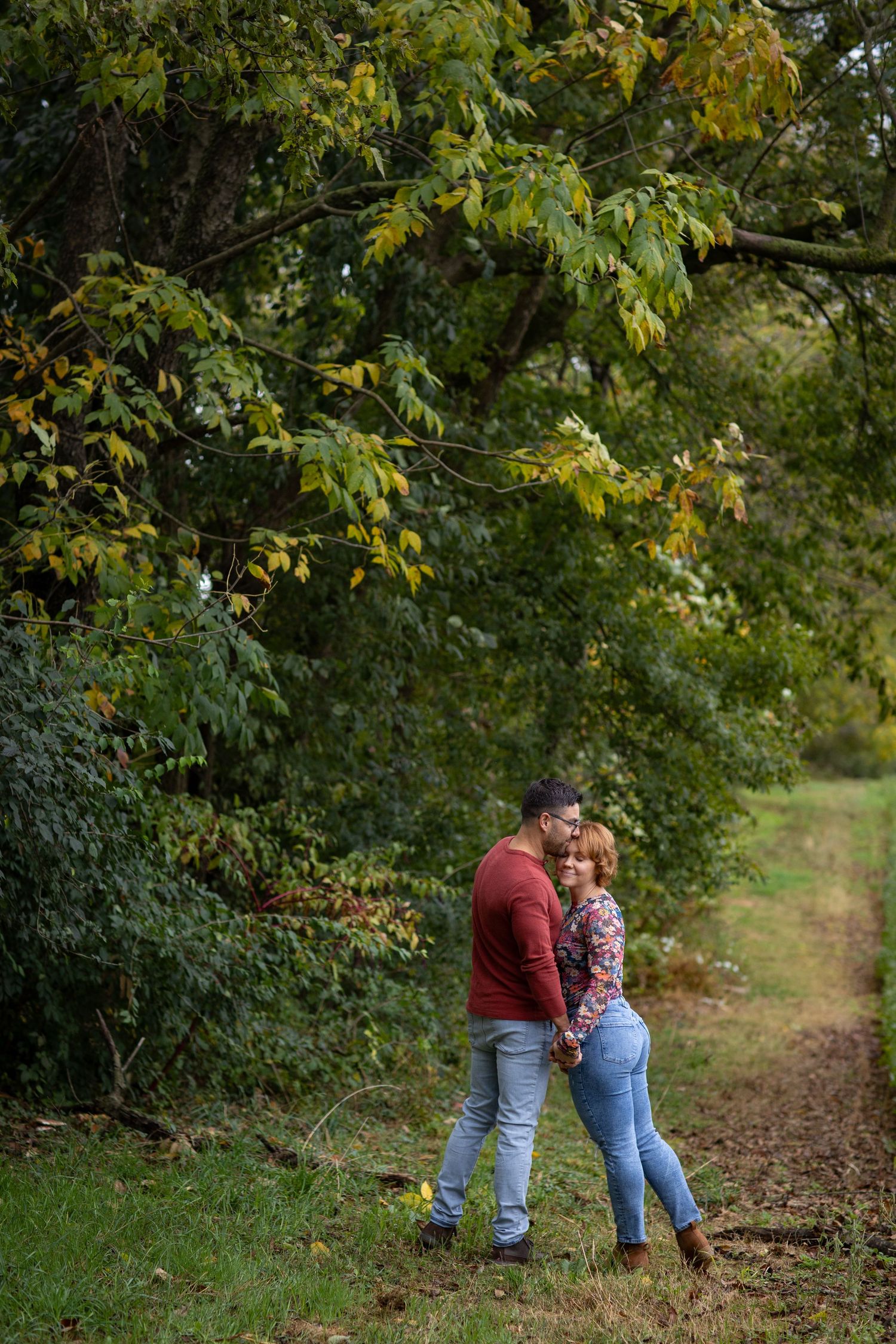 Couple walking along a tree-lined path with autumn leaves creating a romantic outdoor scene.