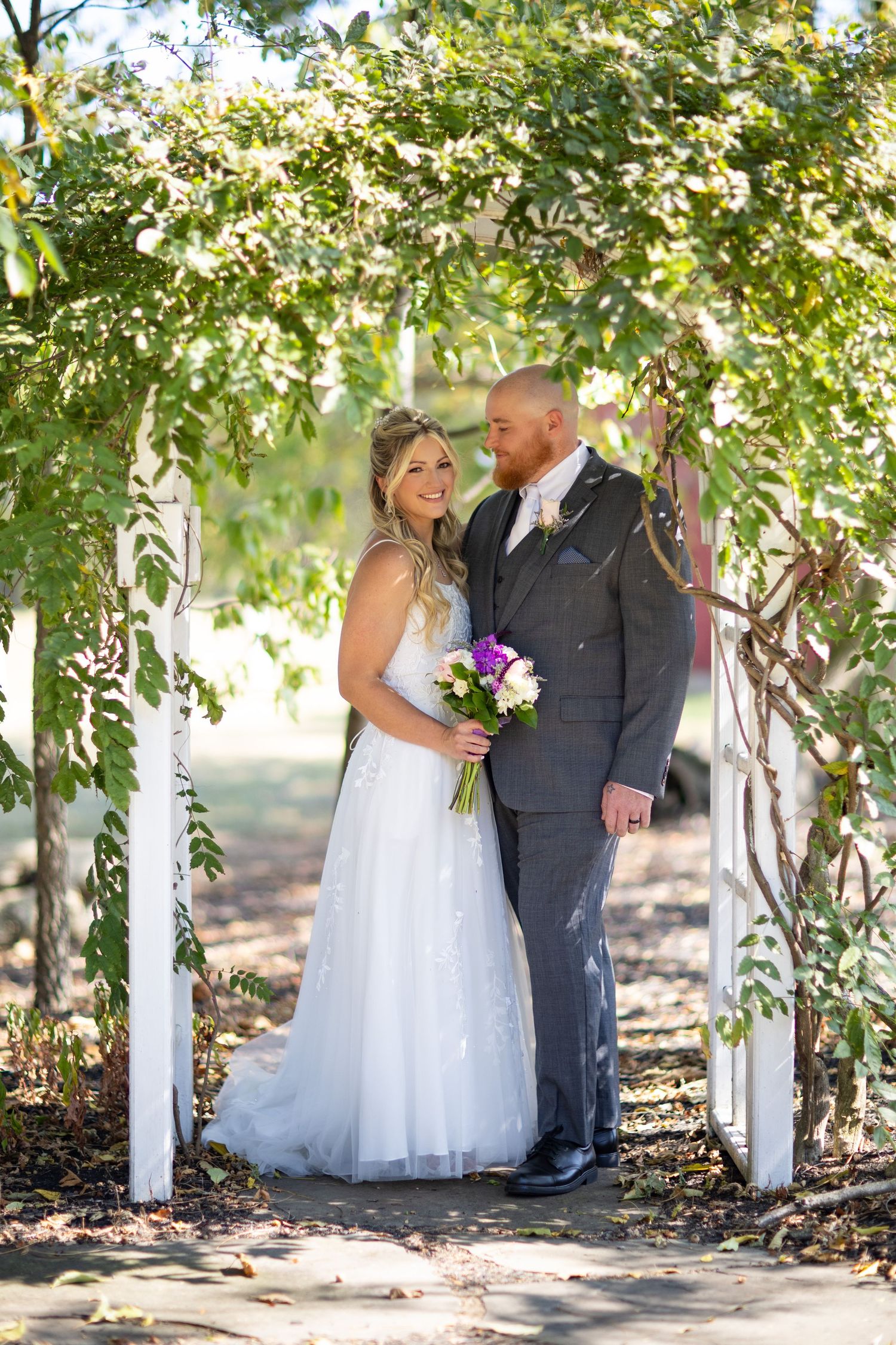 Romantic wedding couple sharing tender moments under a lush garden arbor in natural outdoor setting.