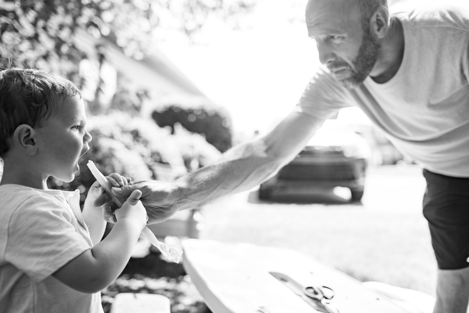 A tender black and white moment shows a young child and adult sharing a playful outdoor interaction.