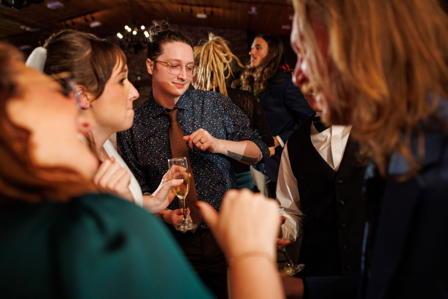 Wedding guests mingle and converse at indoor reception holding champagne glasses.