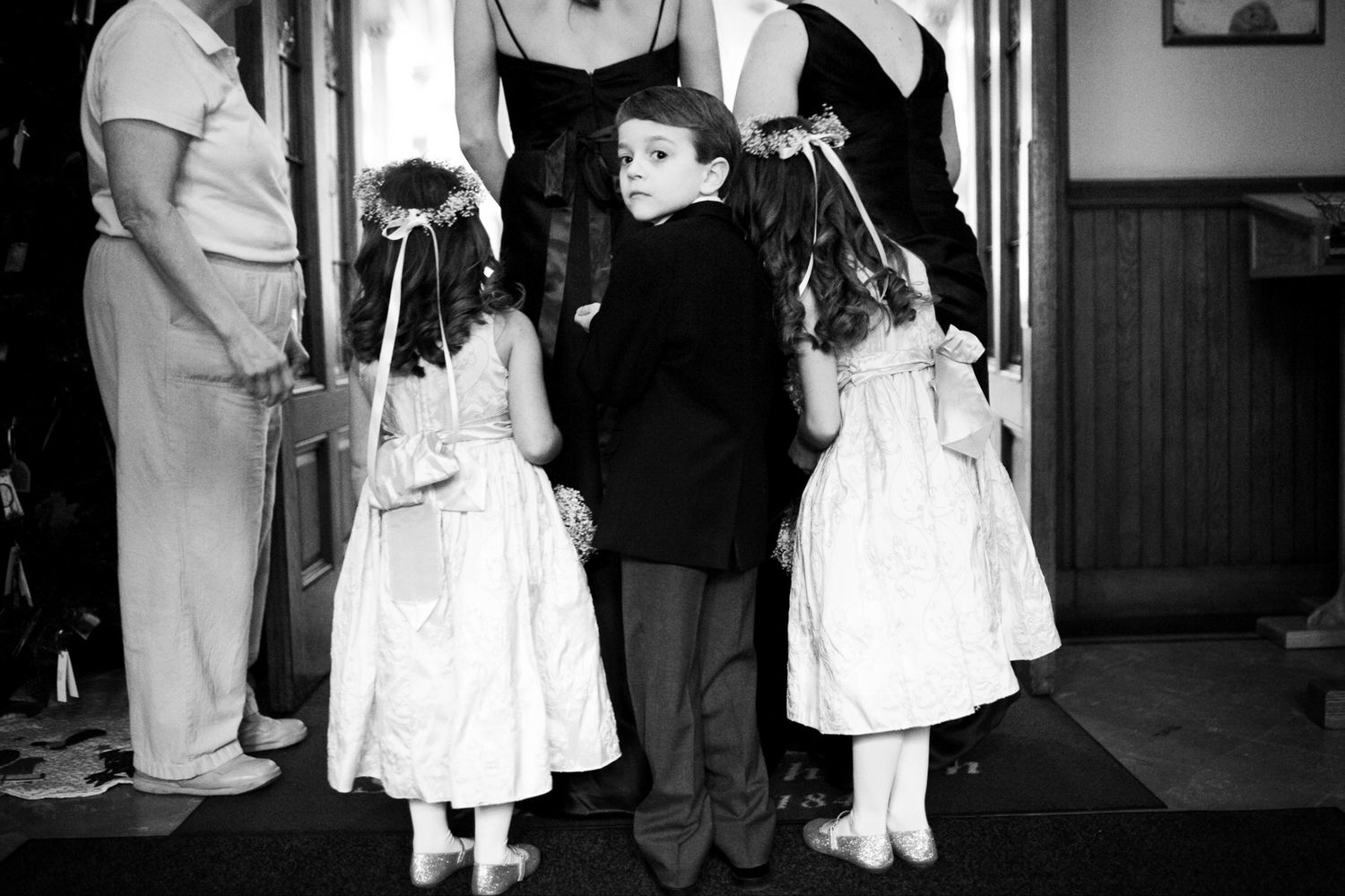 A vintage black and white photograph shows two young girls in white dresses standing with someone in dark clothing.