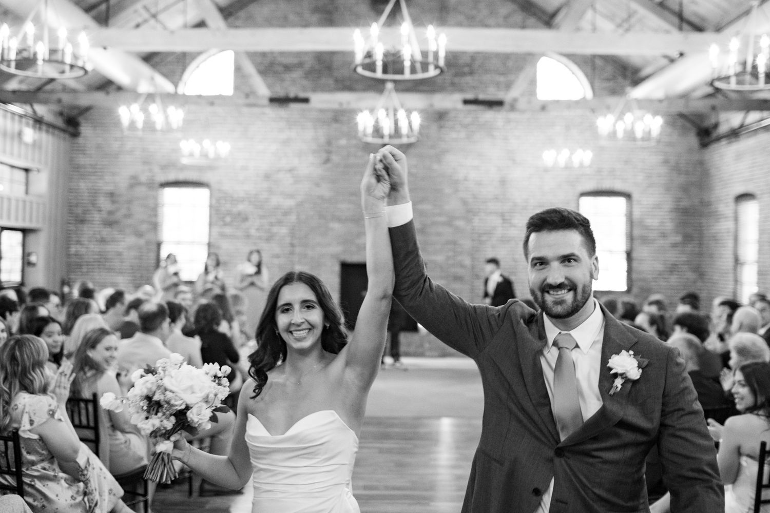 Newlyweds raising hands in celebration as they walk down the aisle after wedding ceremony.
