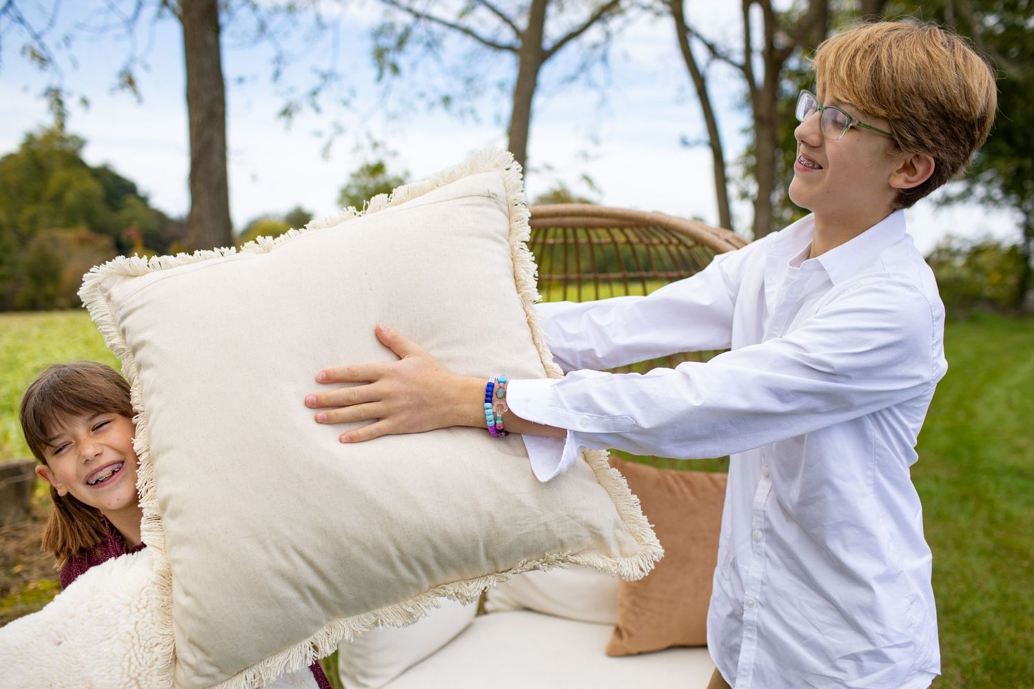 Children in white shirts having a playful pillow fight outdoors on a sunny day.