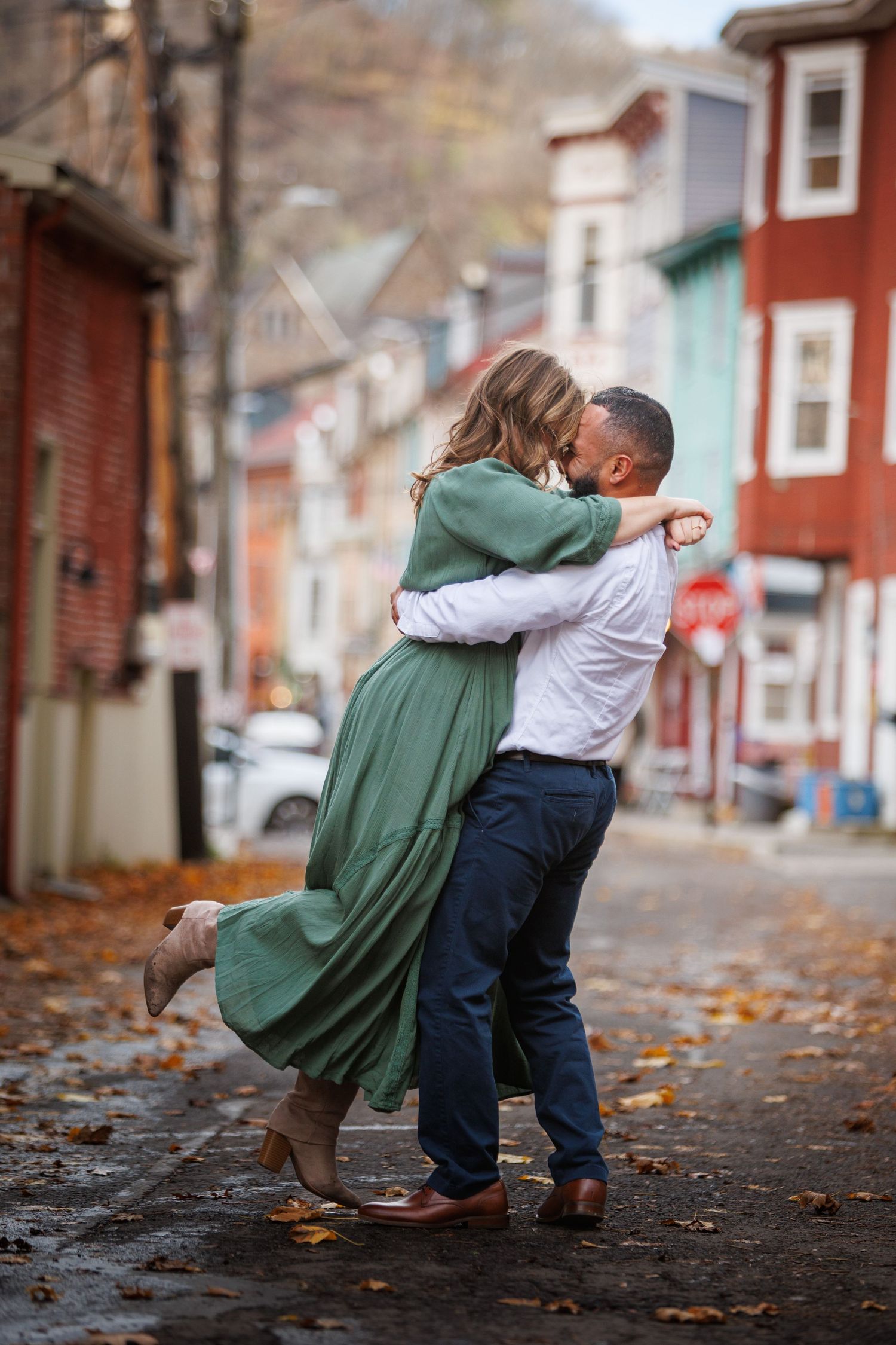 An engaged coupled in casual clothing walking together on a leaf-covered sidewalk in autumn.