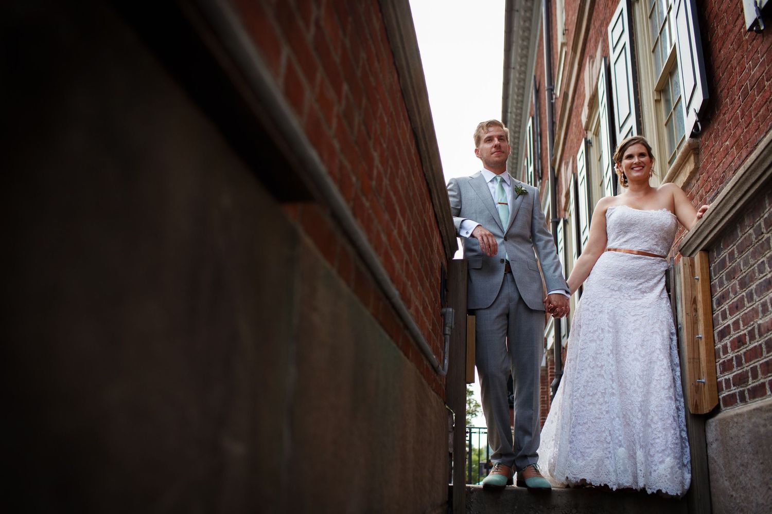 Architectural wedding photo of couple standing on brick building ledge.