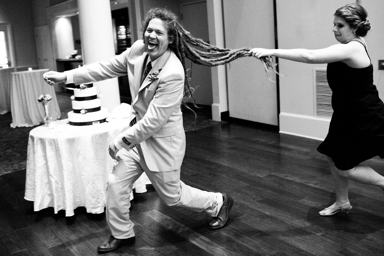 A joyful dance moment captured in black and white at a wedding reception next to a tiered cake.