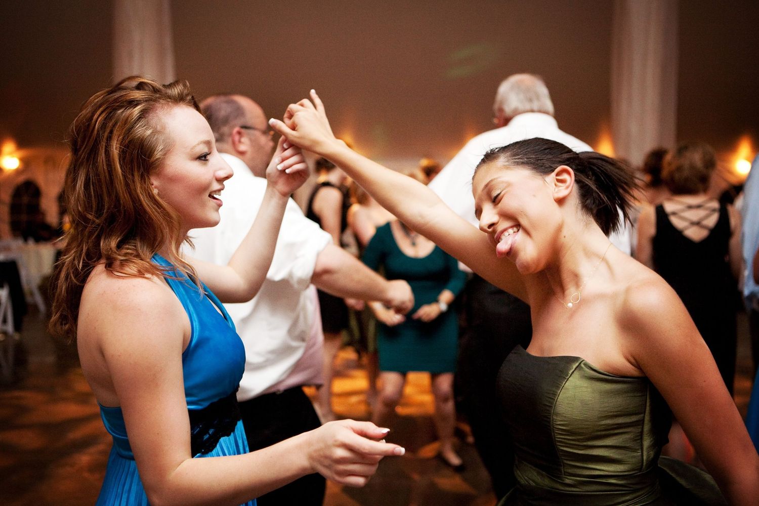Two people dancing energetically and laughing at a celebration on a crowded dance floor.