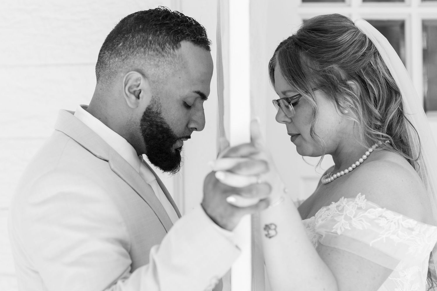 Black and white photo of bride and groom sharing an intimate moment at a white pillar during wedding.