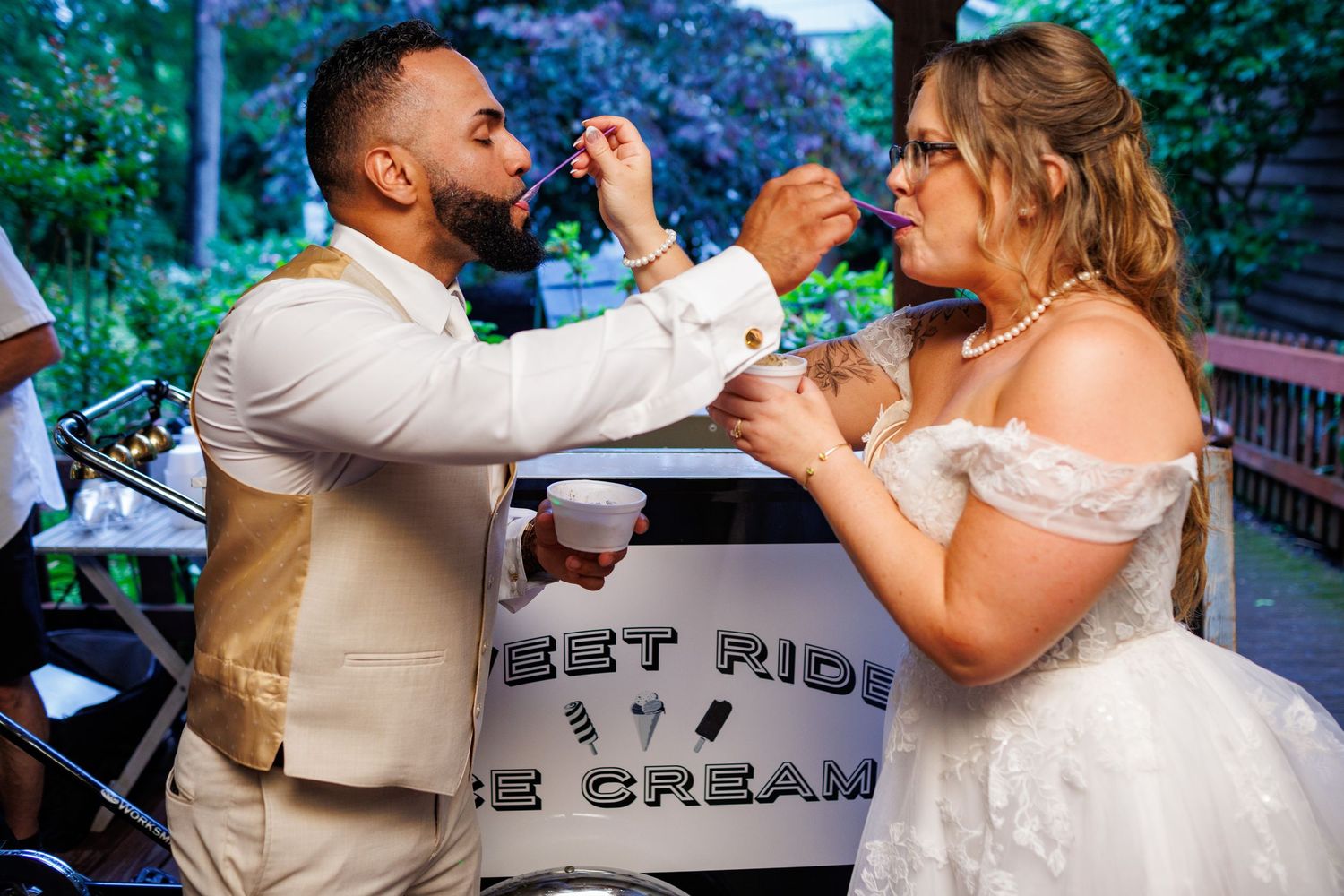 Bride and groom share ice cream from a Sweet Ride Ice Cream cart during wedding reception.