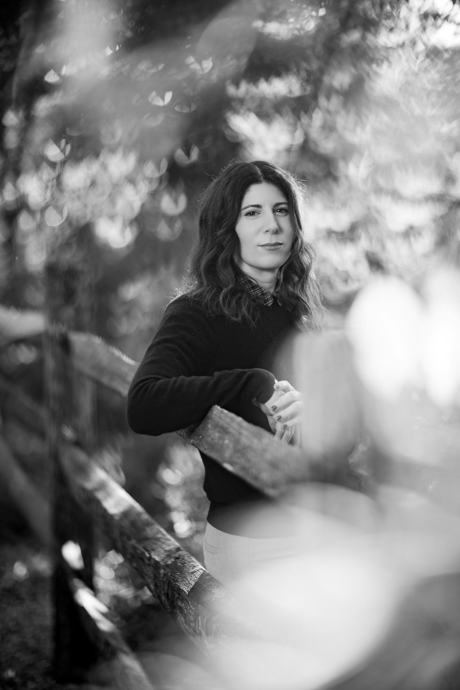 Artistic black and white portrait series through foliage showing woman in dark sweater with ethereal bokeh effects.