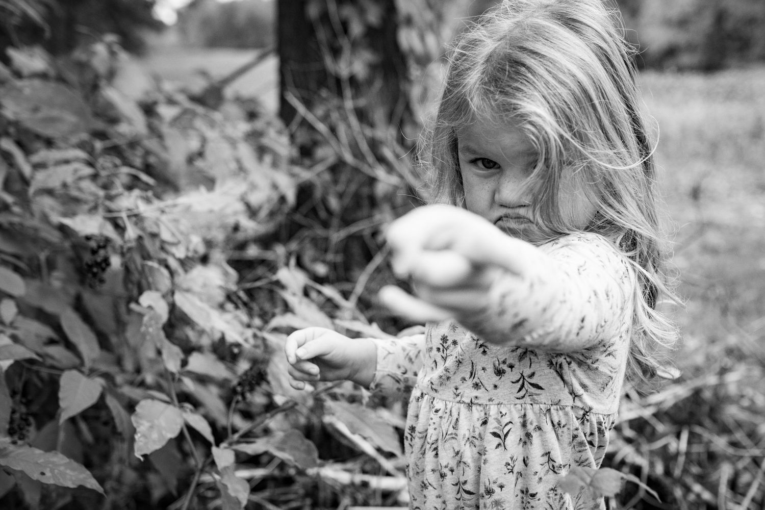 A child explores nature while wearing a floral dress outdoors.