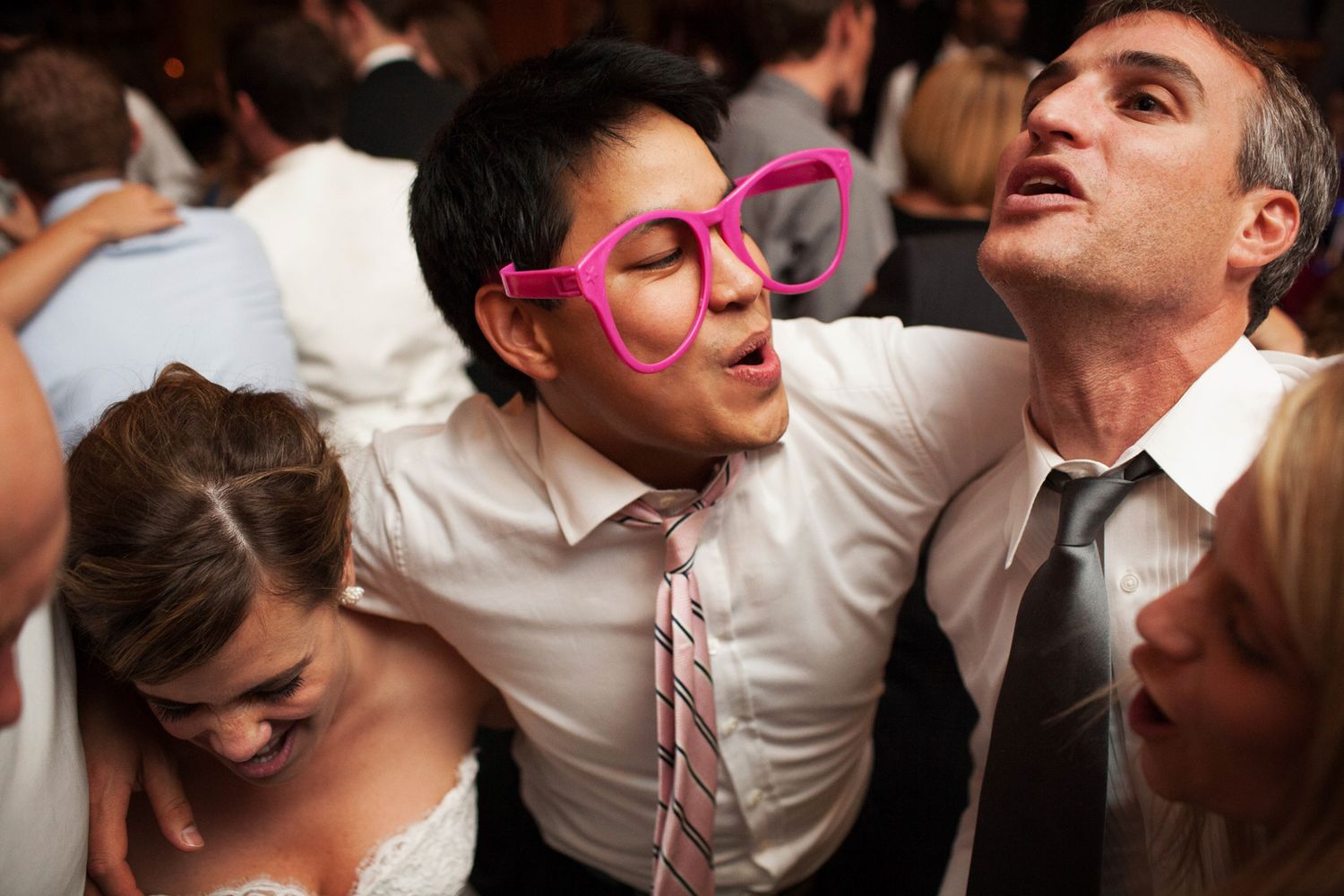 huge pink glasses on the face of a man dancing with his friends at a wedding