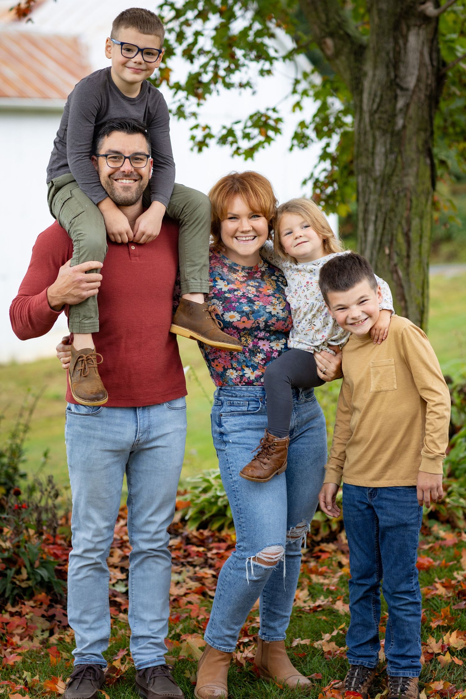 A family group poses together outdoors among fallen autumn leaves.