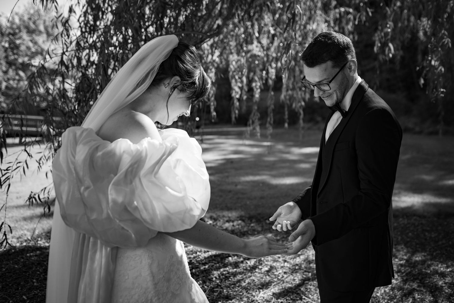 Black and white photo of bride and groom holding hands outdoors near a pond on their wedding day.