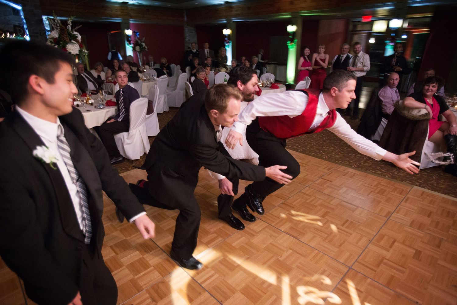 Wedding guests performing a synchronized dance routine on a parquet dance floor at a reception.