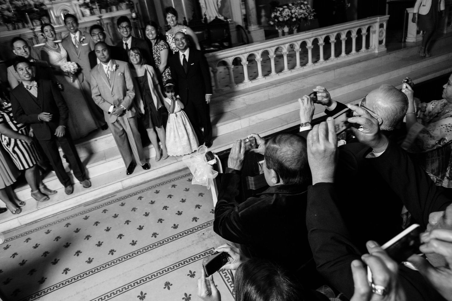 Black and white photo of photographers with cameras capturing a scene on an ornate staircase with patterned floor.