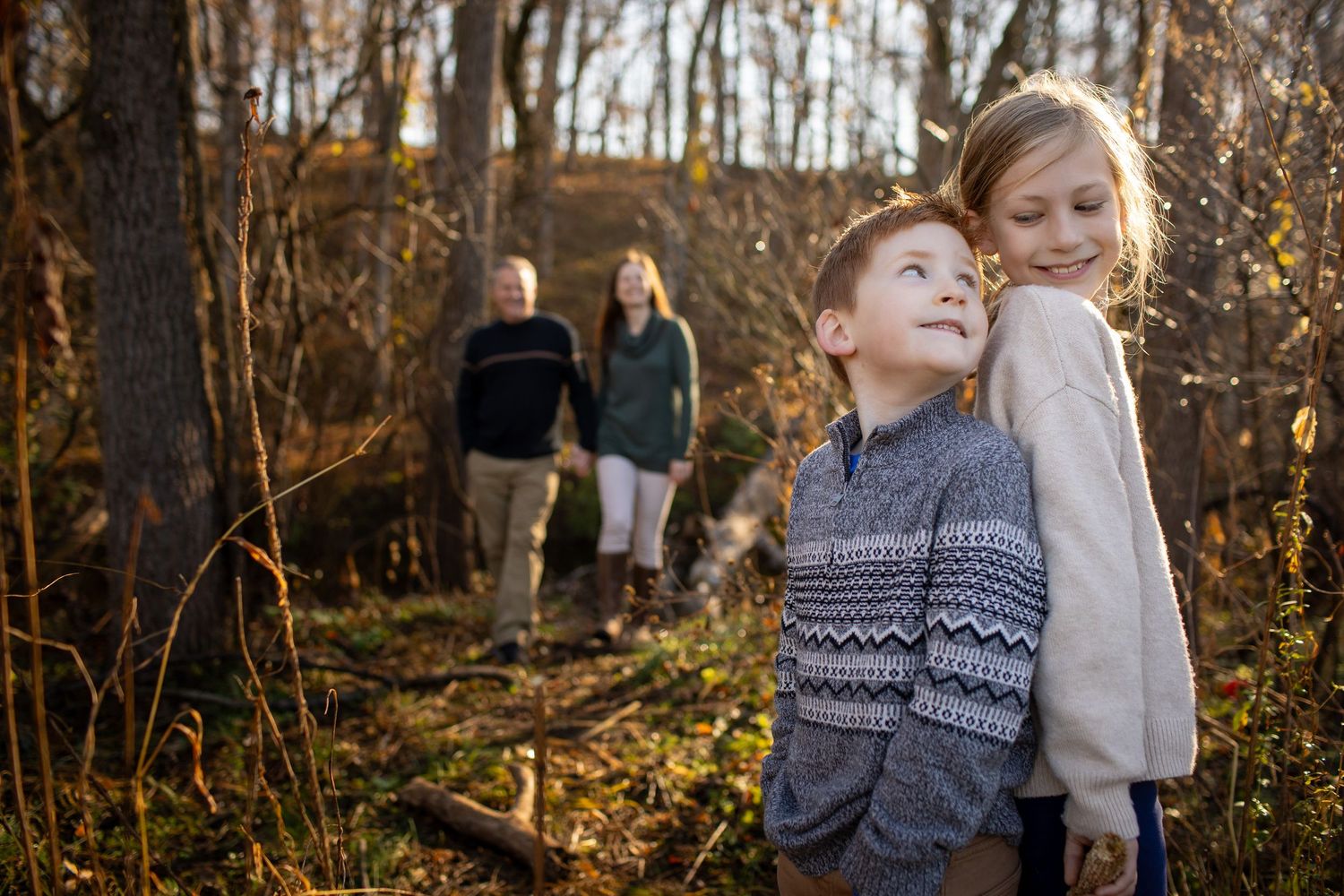 A couple enjoys a romantic autumn photoshoot in a wooded area with golden sunlight filtering through trees.