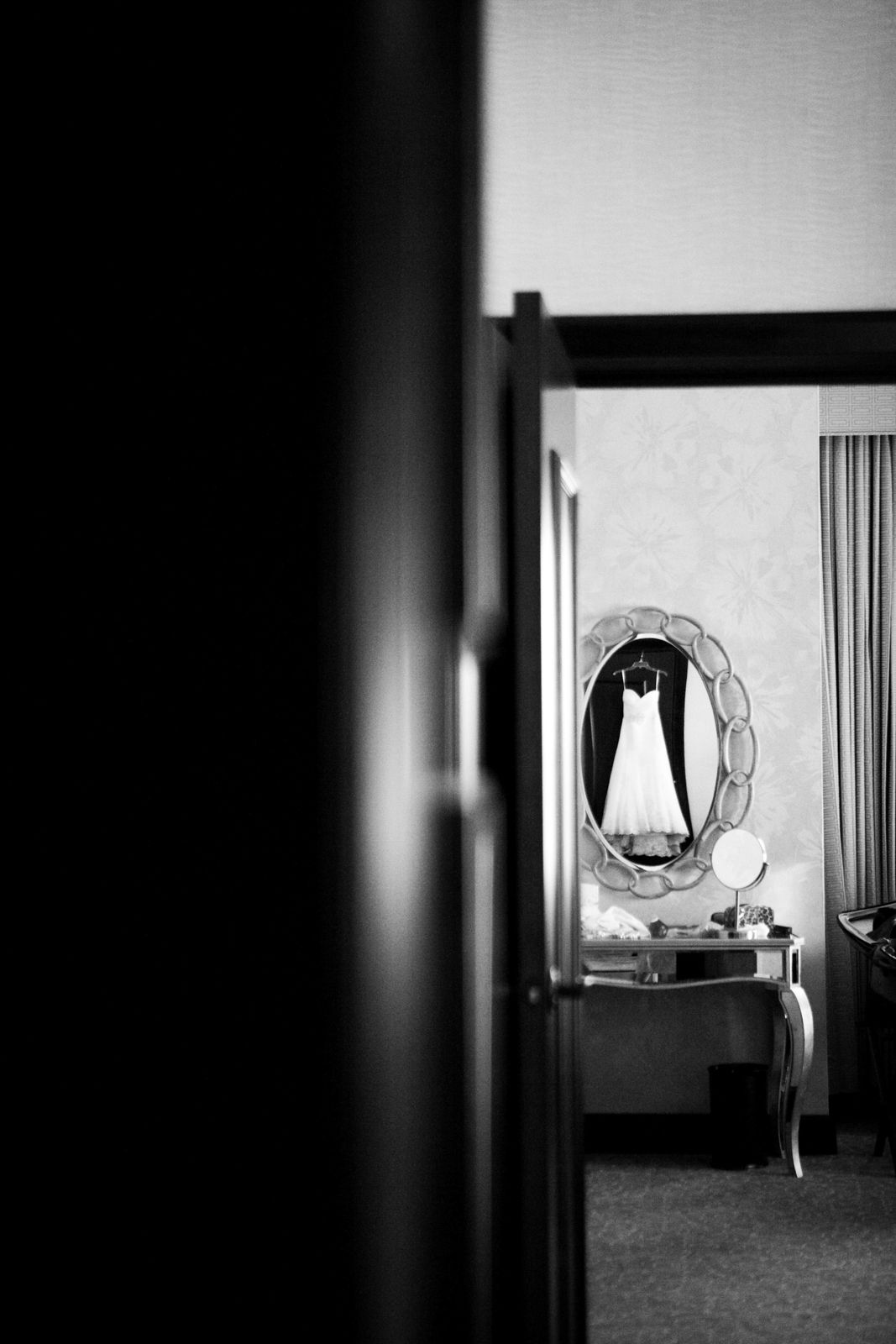 An image of a wedding dress hanging through a doorway. This is a black and white image