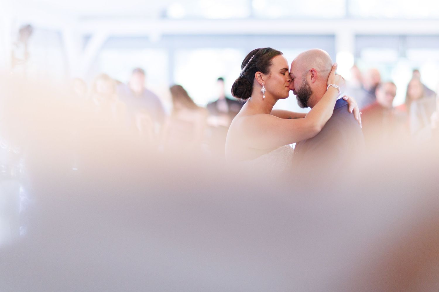 A couple shares a tender moment during their first dance at an indoor wedding reception.