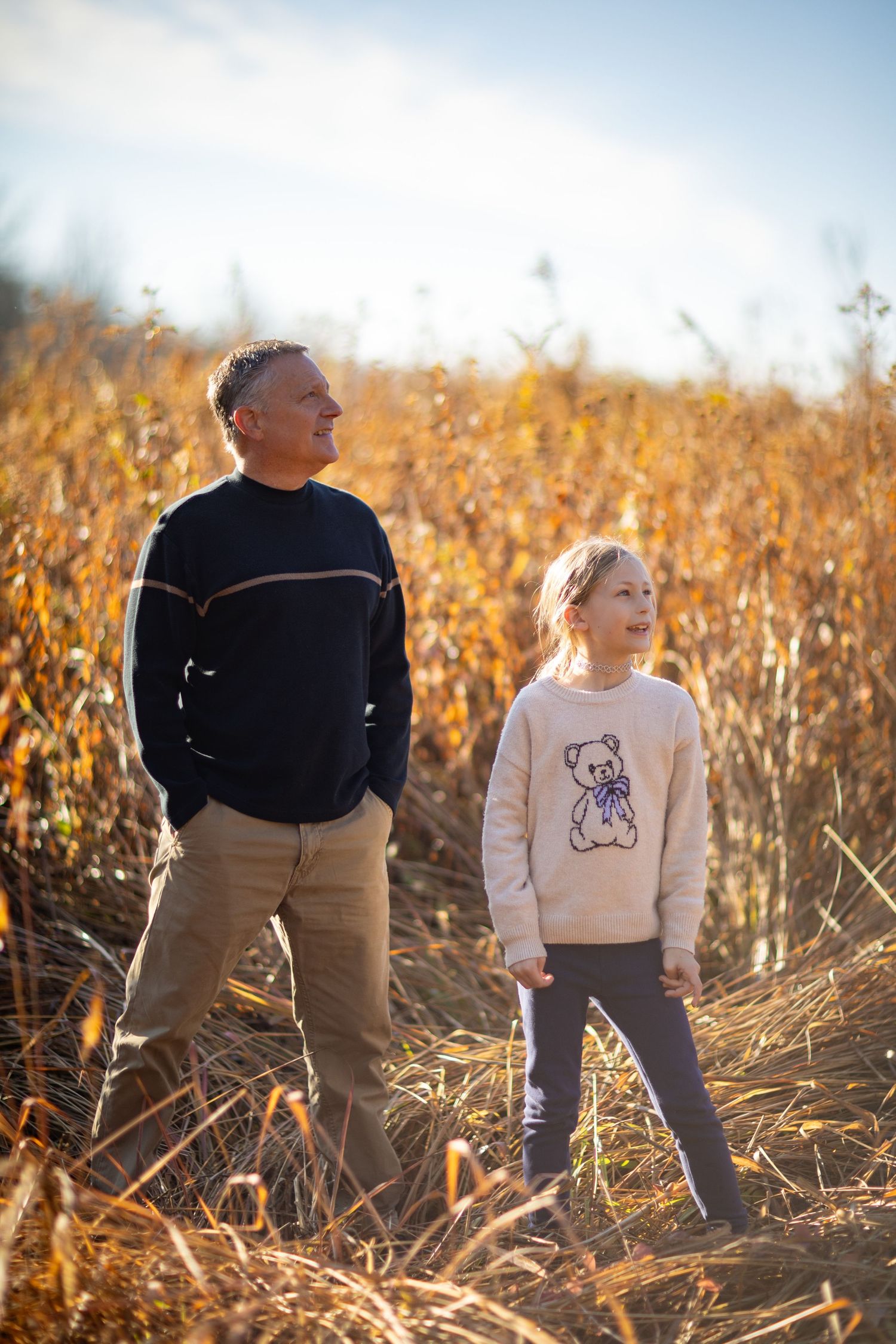 Two people play together in a golden autumn cornfield at sunset creating playful silhouettes.